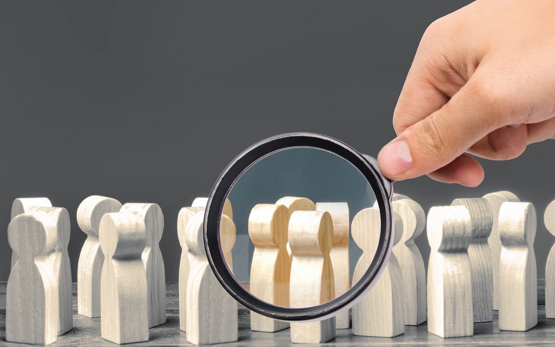 A magnifying glass looks at a crowd of wooden figures (as symbolic representation of segmentation in email marketing)